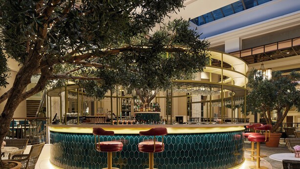A bar area with a curved counter, multiple stools, and a large tree in the center.