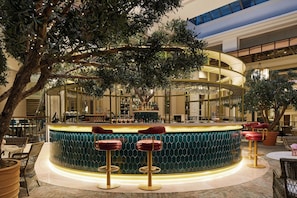 A bar area with a curved counter, multiple stools, and a large tree in the center. - The Midland - Manchester (Manchester)