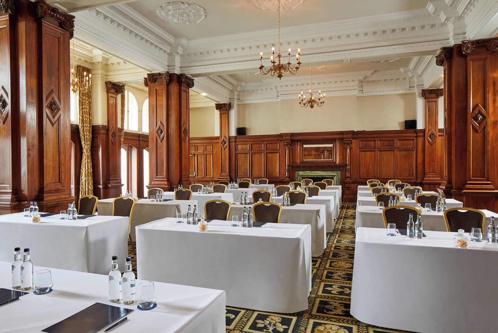 A formal banquet hall with multiple round tables, each set with white tablecloths, chairs, and water bottles.