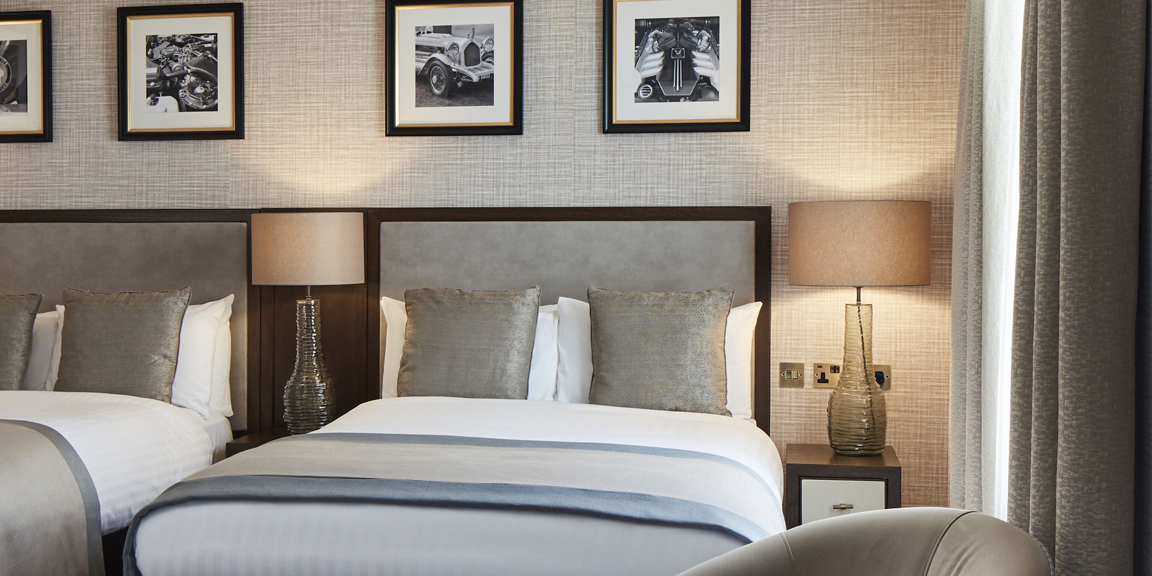 Une chambre d’hôtel avec deux lits, une grande tête de lit, une table de chevet avec une lampe et des tableaux encadrés au mur.