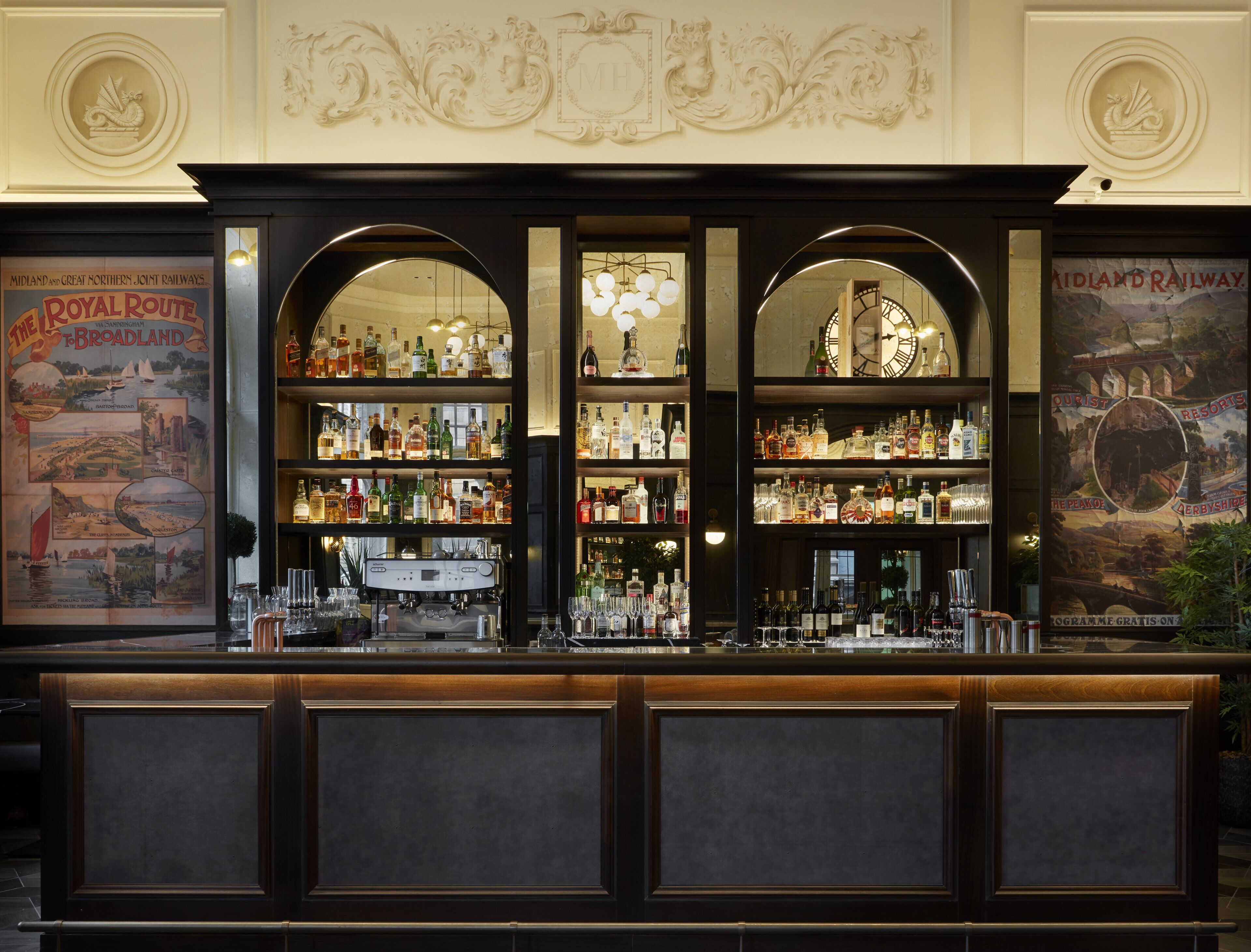 A bar with a vintage design, featuring a clock, multiple shelves of bottles, and a decorative wall above.