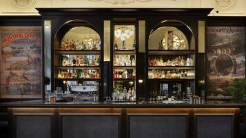 A bar with a vintage design, featuring a clock, multiple shelves of bottles, and a decorative wall above.