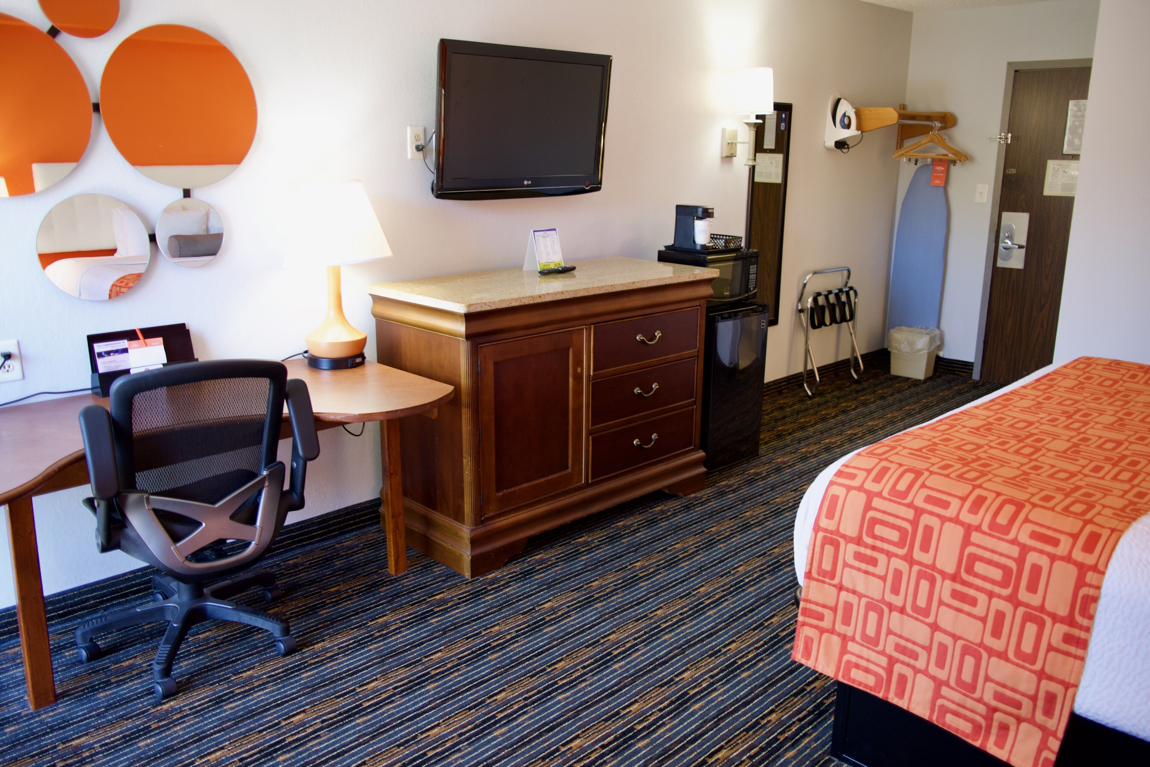 A hotel room with a bed, a desk with a chair, a television, a coffee machine, and a mirror.