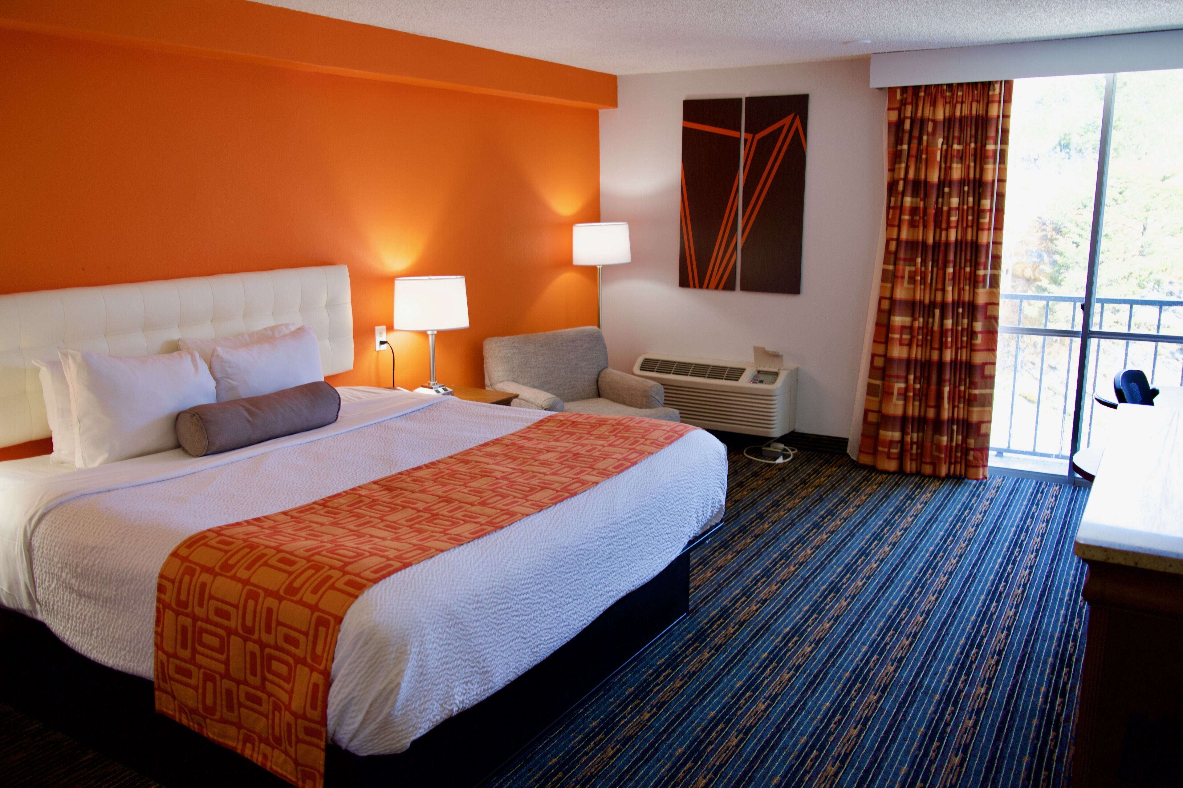 Une chambre d’hôtel avec un grand lit, deux lampes de chevet, un bureau, une chaise, un climatiseur et une fenêtre avec des rideaux.