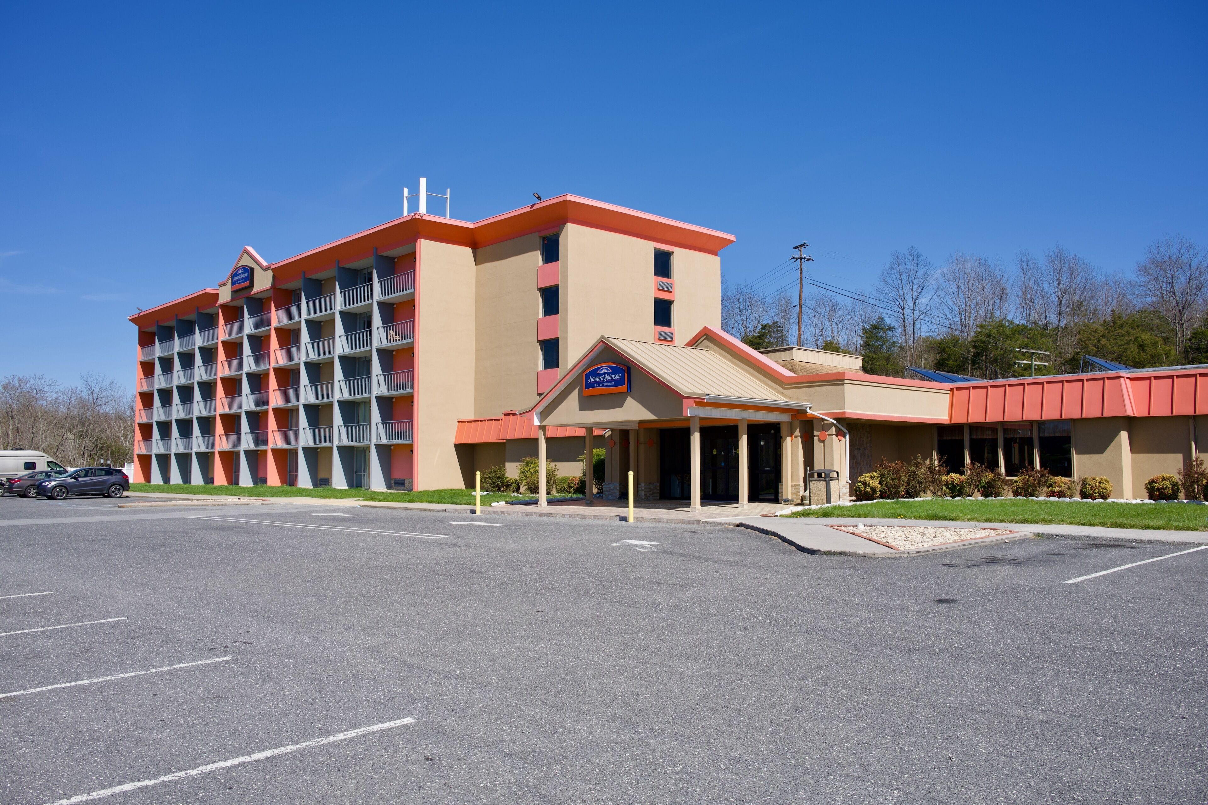 Un hotel de varios pisos con fachada roja y beige, un acceso cubierto y un estacionamiento.