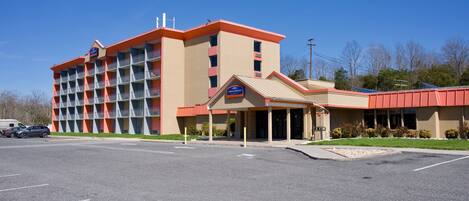 A multi-story hotel with a red and beige exterior, a covered entrance, and a parking lot.