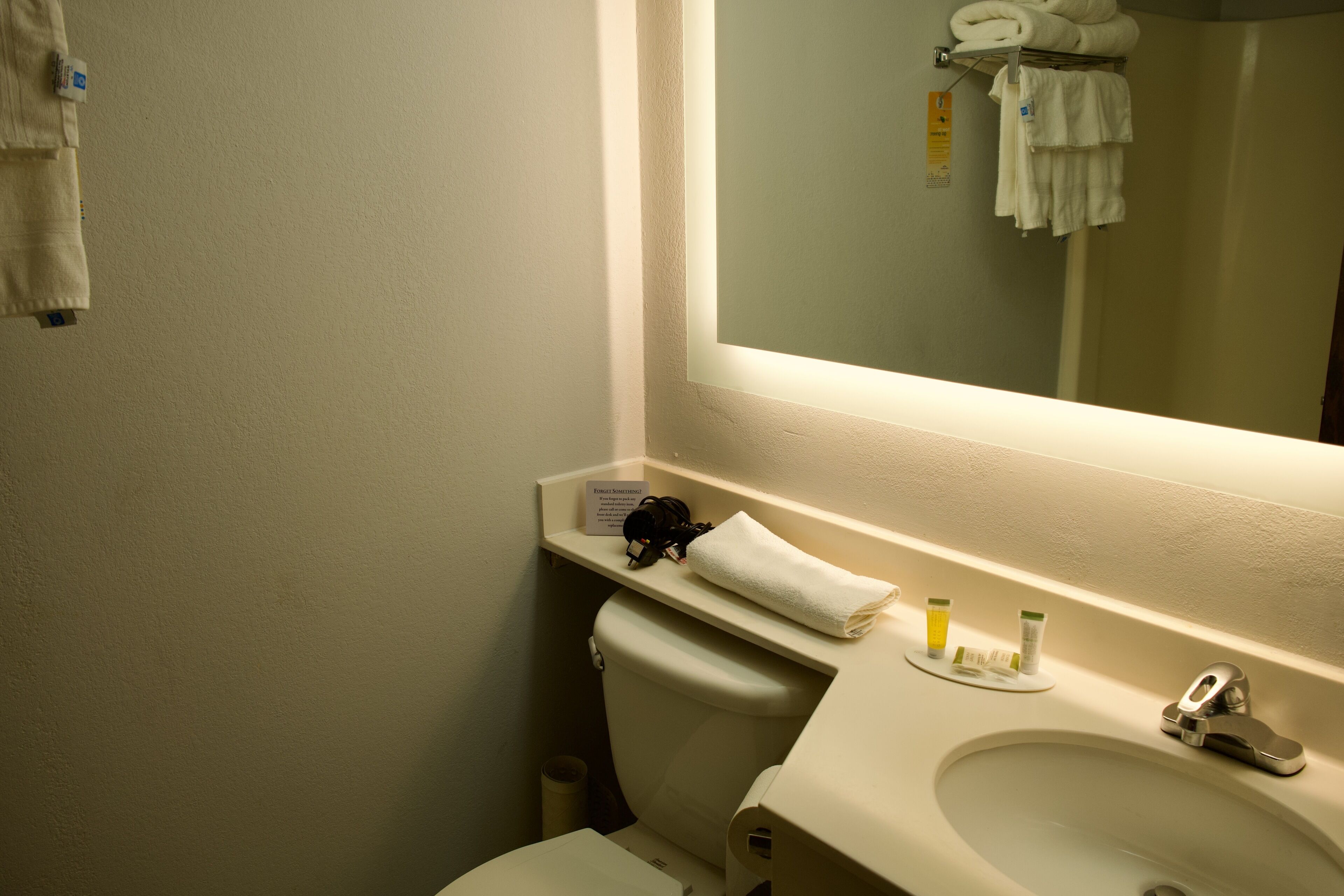 A bathroom with a white sink, mirror, and toilet. There are towels and toiletries on the sink counter.