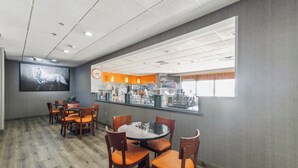 A conference room with a round table and chairs, a large screen, and a kitchen area visible through a window. - Howard Johnson by Wyndham Lexington (Lexington)