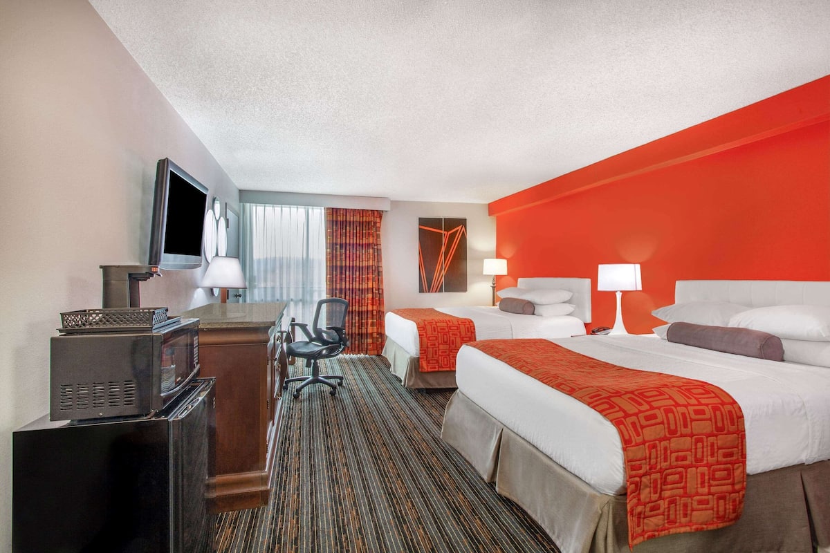 A hotel room with two beds, a desk with a TV, a chair, and a microwave.