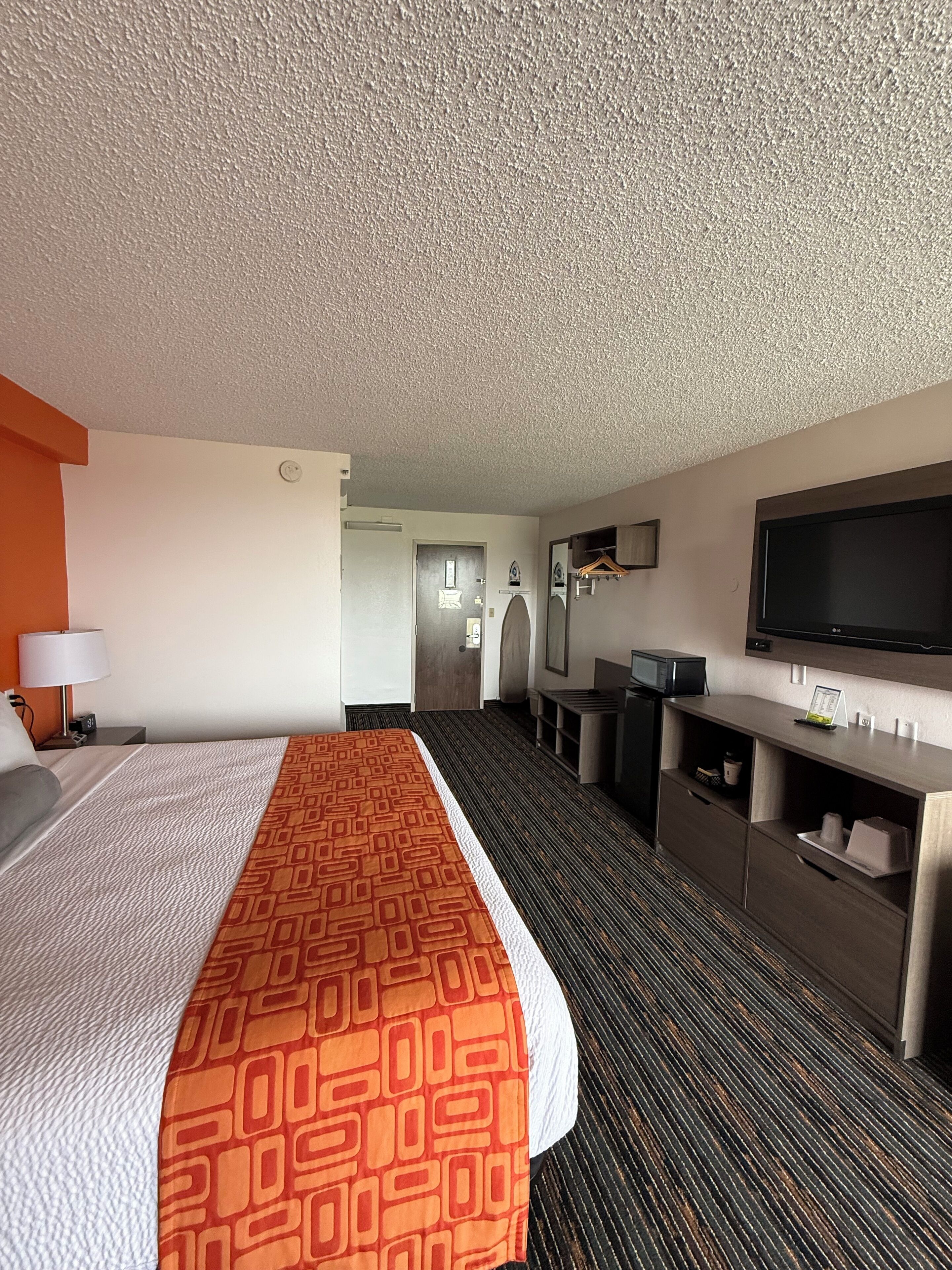A hotel room with a large bed, a desk, a flat-screen TV, and a walk-in closet.
