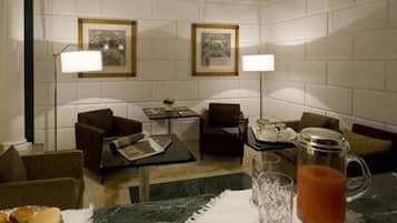 A hotel room with a marble floor, two armchairs, a small table, a coffee table, a lamp, a picture frame, and a pitcher of tea.