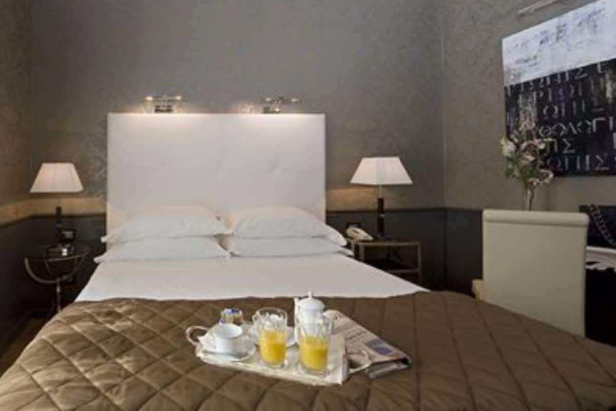Une chambre d’hôtel avec un grand lit, deux tables de chevet, une petite table, une lampe fixée au mur et un plateau contenant des articles pour le petit-déjeuner.