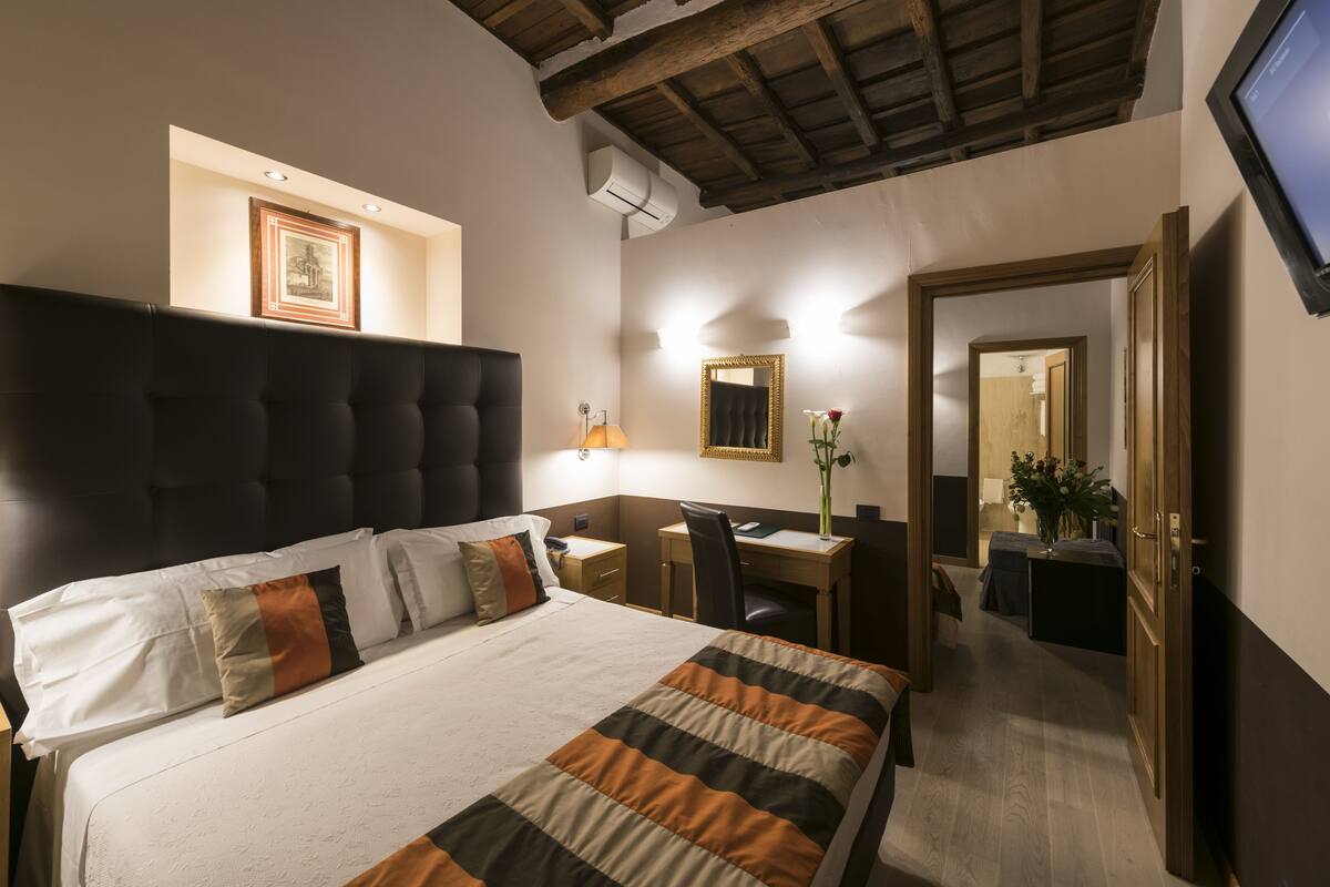 A hotel room with a large bed, a desk, a chair, a mirror, and a TV.