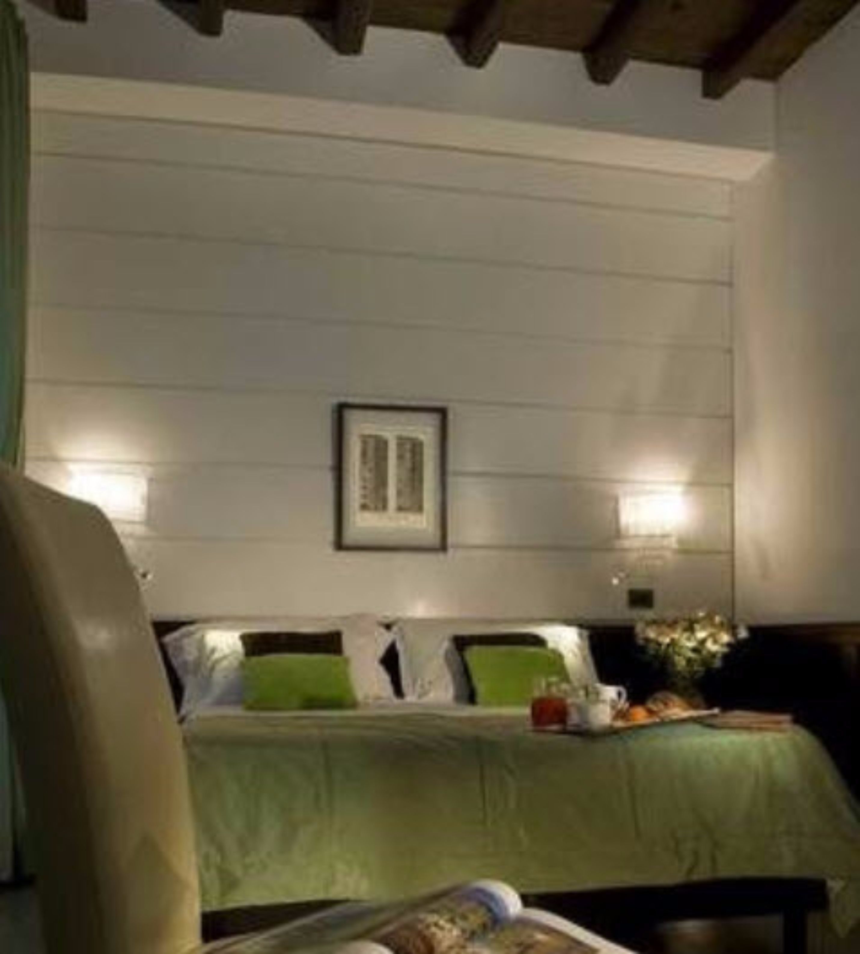 Quarto com cama, almofadas, um quadro na parede e duas luminárias.