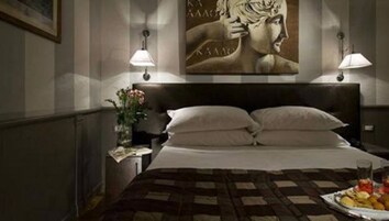A hotel room with a large bed, two bedside lamps, a nightstand with a vase of flowers, and a painting on the wall.