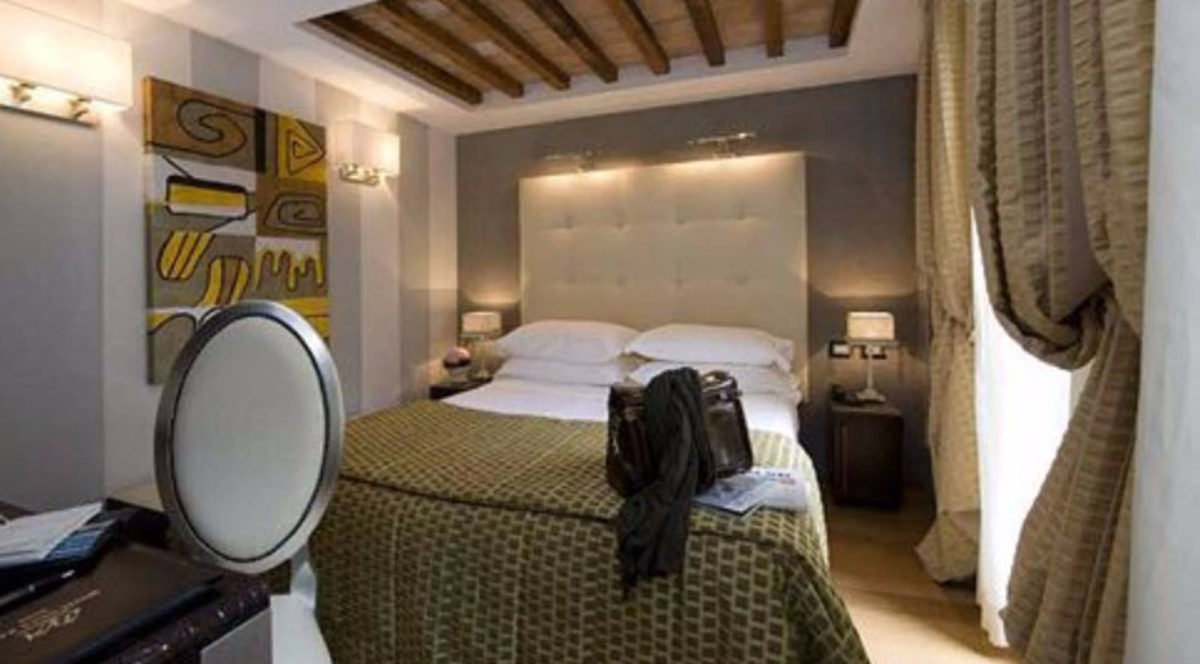 A hotel room with a bed, bedside tables, a mirror, and a wall with abstract art.
