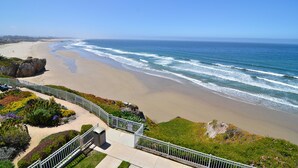 Vista costera con playa, olas del océano y un muelle que se adentra en el agua.