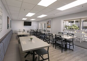 A conference room with a long table, multiple chairs, a bench, and a large window overlooking a balcony with outdoor seating. - Pismo Lighthouse Suites (Pismo Beach)