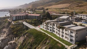 Un hotel costero con varias edificaciones, un puente que conecta con la playa y vistas al océano.