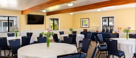 A conference room with round tables, blue chairs, and white tablecloths.
