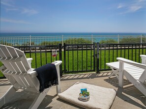 A balcony with two white Adirondack chairs, a small rug, and a bowl with dog treats. - Pismo Lighthouse Suites (Pismo Beach)