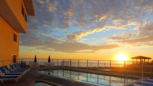 Zona de piscina con sillones de descanso y vista al atardecer sobre el océano.