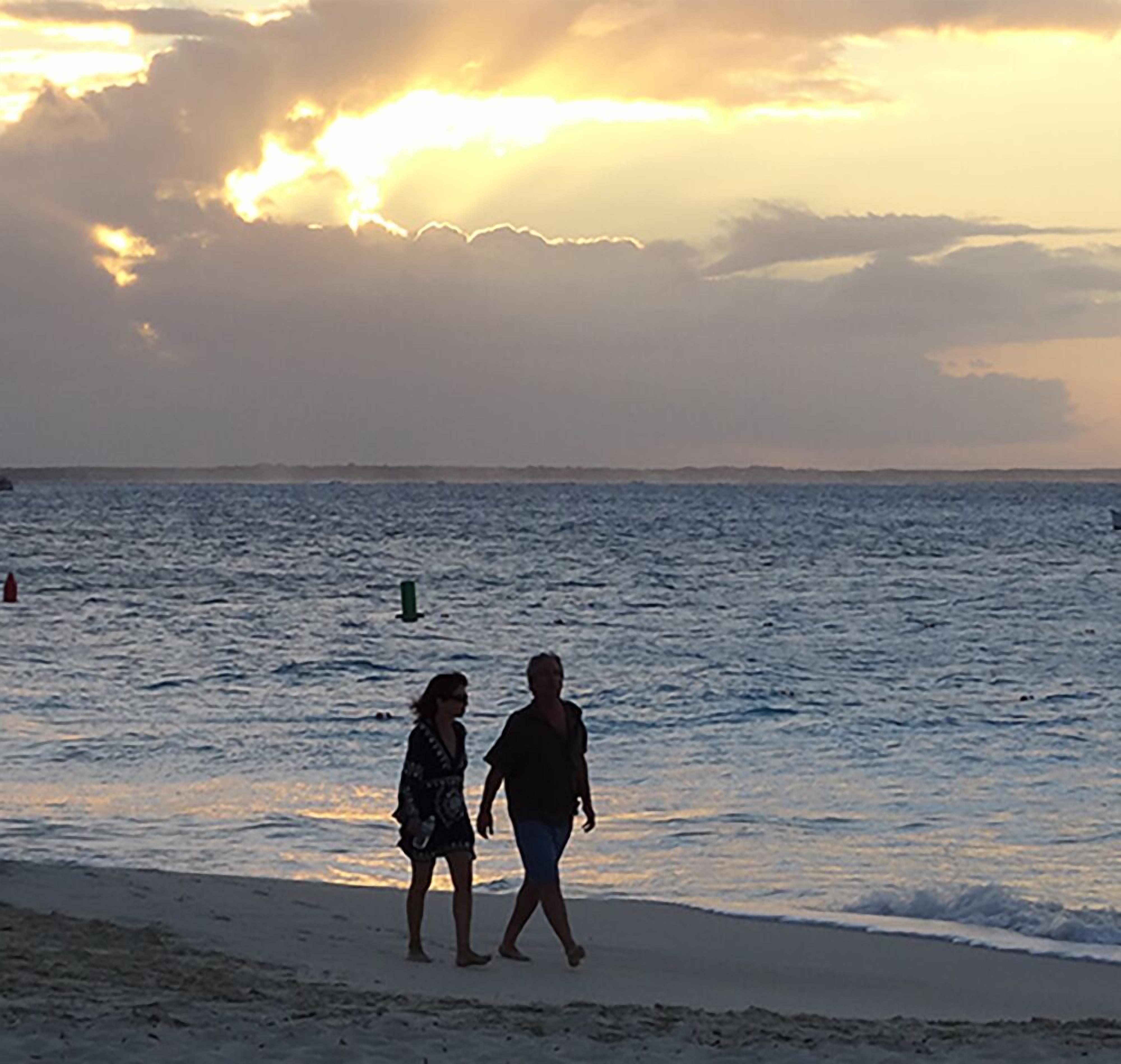 Escena de playa con dos personas caminando por la orilla.
