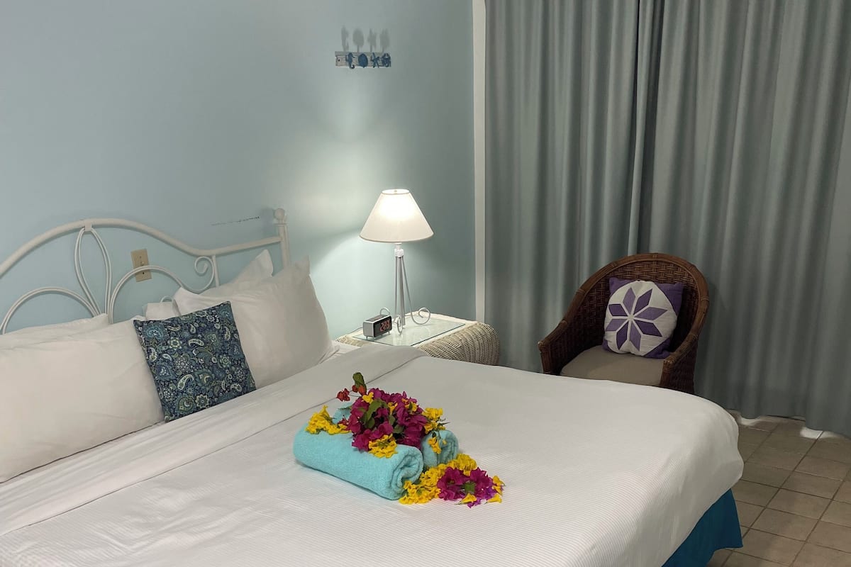 A neatly made bed with a blue skirt, white linens, and a floral arrangement.