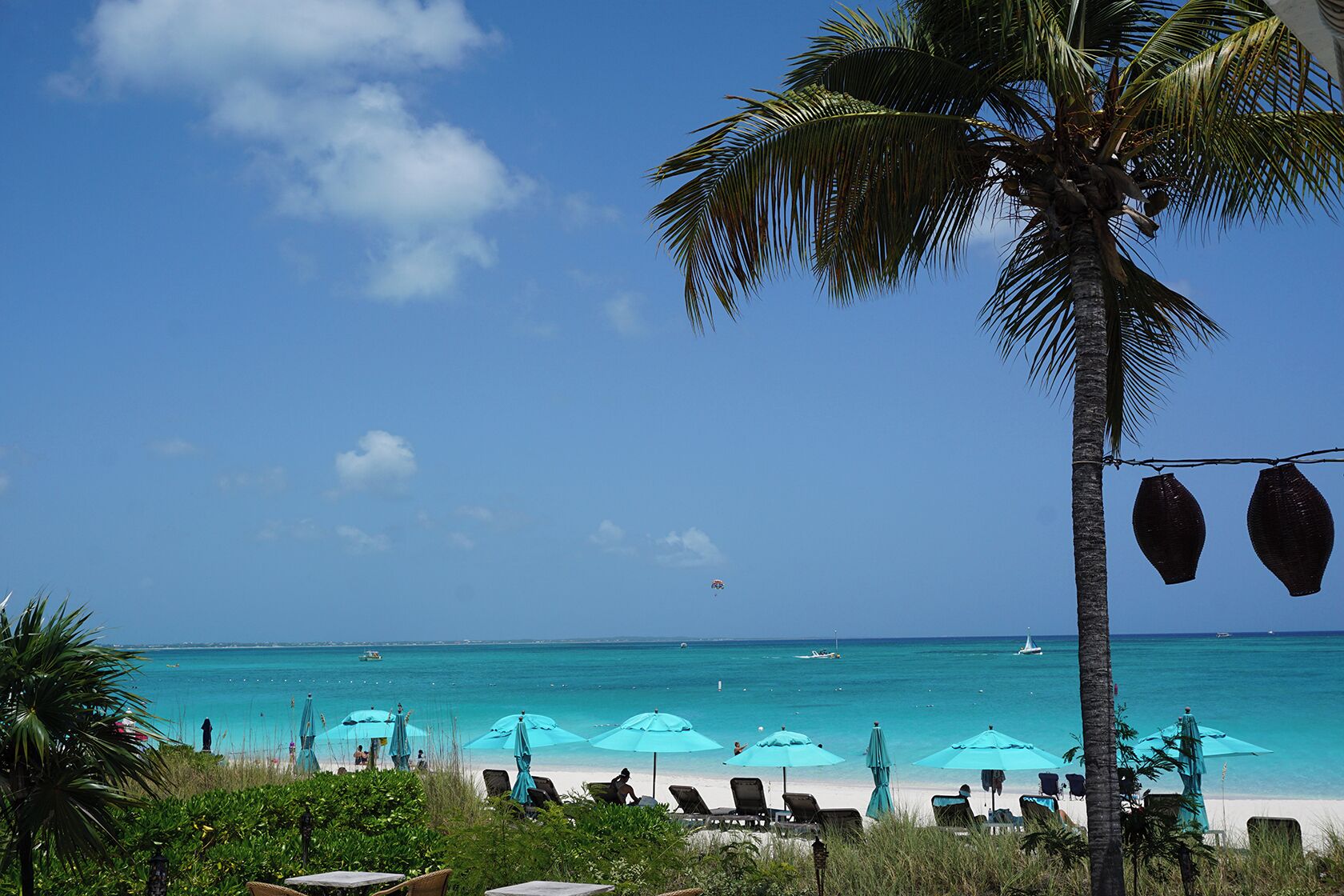 A beach with turquoise water, a clear sky, and several umbrellas and lounge chairs.