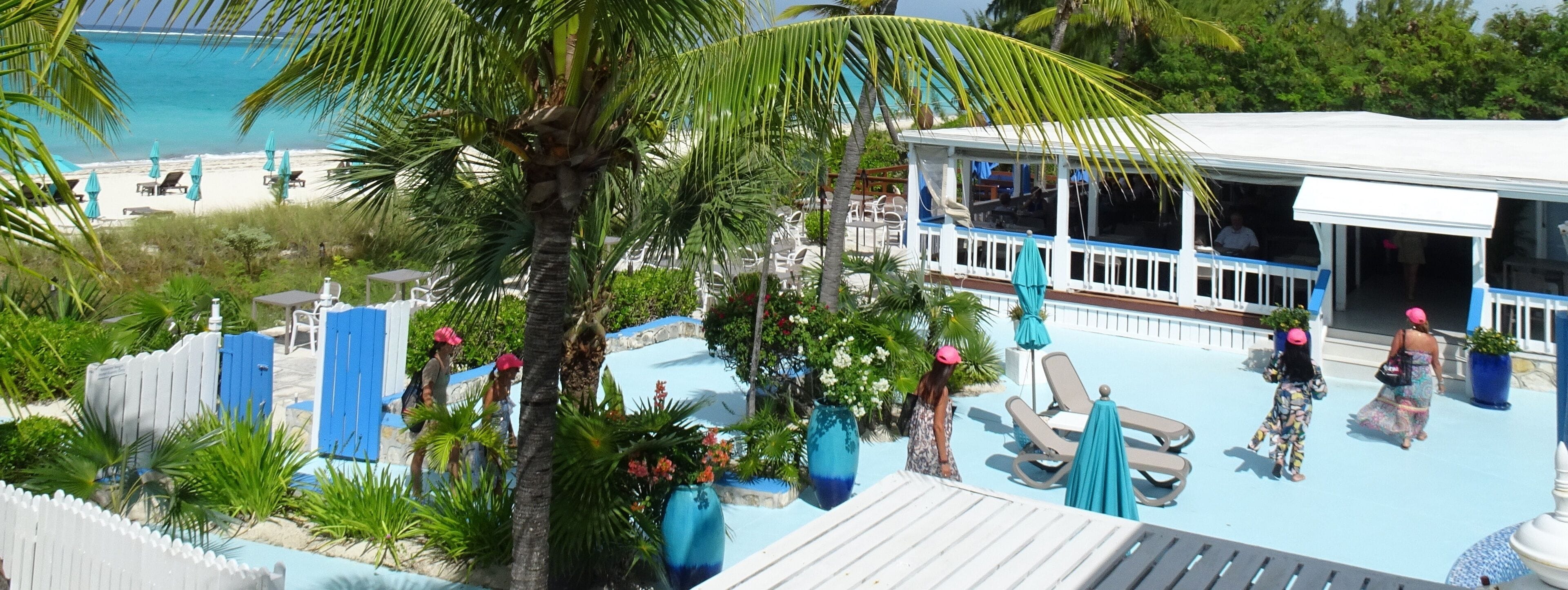 A pool area with lounge chairs and umbrellas, surrounded by palm trees and a view of the beach.