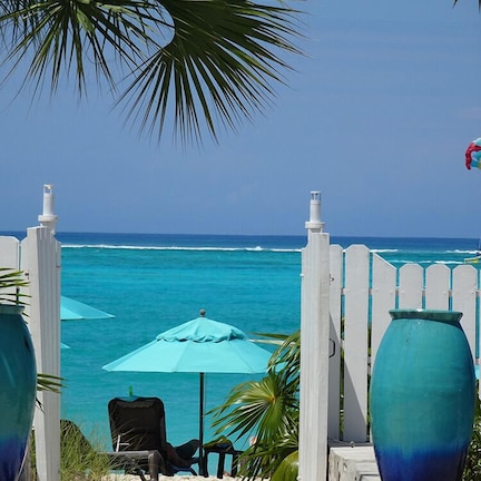 A beach view with a white fence, two large vases, a blue umbrella, and a chair.