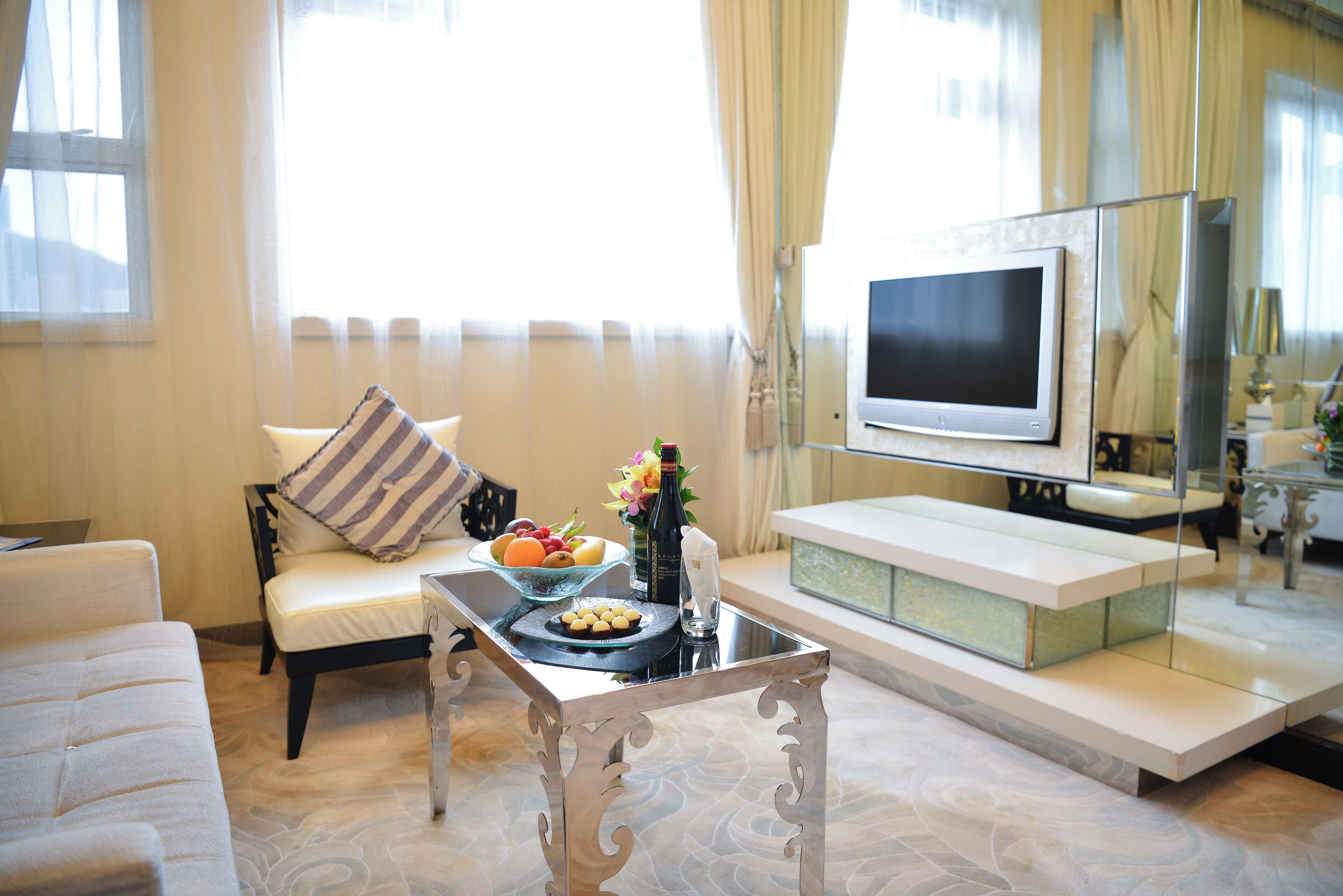 A modern living room with a sofa, a coffee table, a TV, and a dining area with a bowl of fruit and a bottle.
