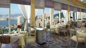 A high-rise dining area with large windows offering a city view. Tables are set with fine dining ware. - Regal Hongkong Hotel (Hong Kong)