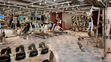 Ett gym med olika typer av träningsutrustning, inklusive löpband, styrketräningsmaskiner och hantlar.
