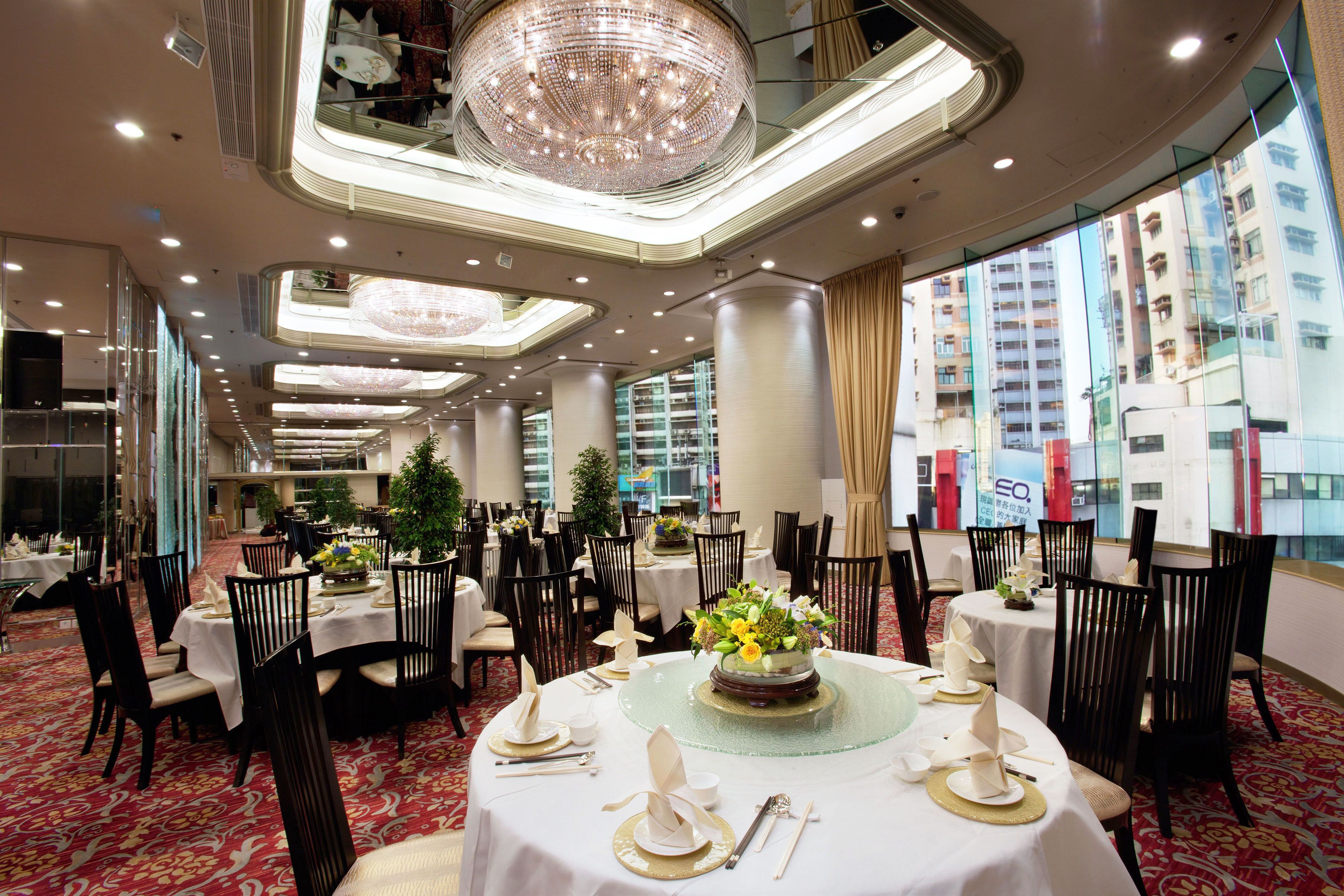 A hotel dining area with round tables, black chairs, and a chandelier.