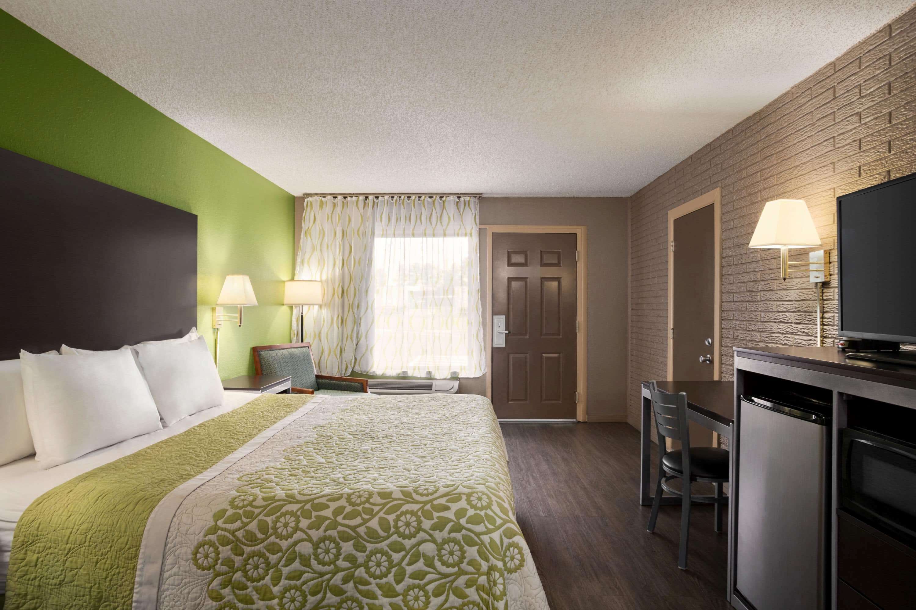 A hotel room with a bed, a desk, a chair, a television, and a door.