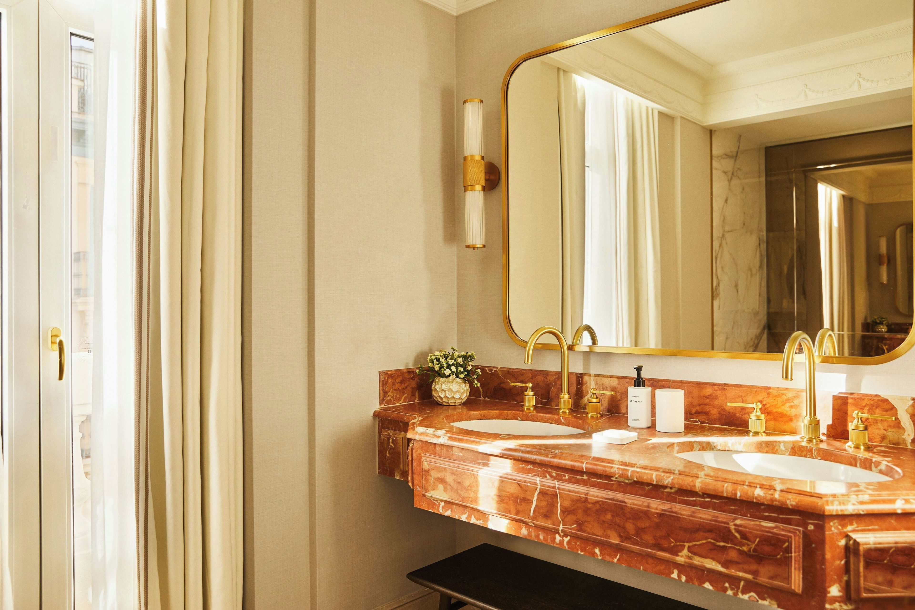 A bathroom with two sinks, a large mirror, and a vase with flowers.