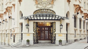 Una entrada imponente con intrincados trabajos de hierro forjado y un gran puerta central, flanqueada por columnas y detalles decorativos.