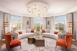 Un salón amplio con un sofá blanco grande, dos sillones naranjas, una mesa de centro de madera y una lámpara decorativa.