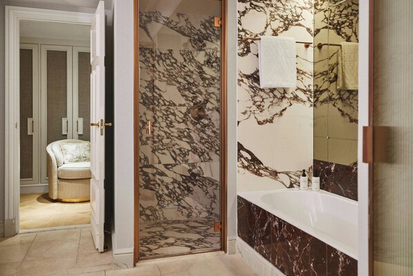A bathroom with a marble shower, a bathtub, and a mirror.
