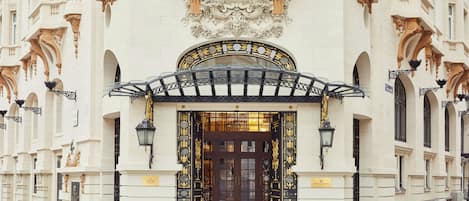A grand entrance with a black iron gate, a large ornate sign above the door, and a symmetrical facade with columns and decorative elements.