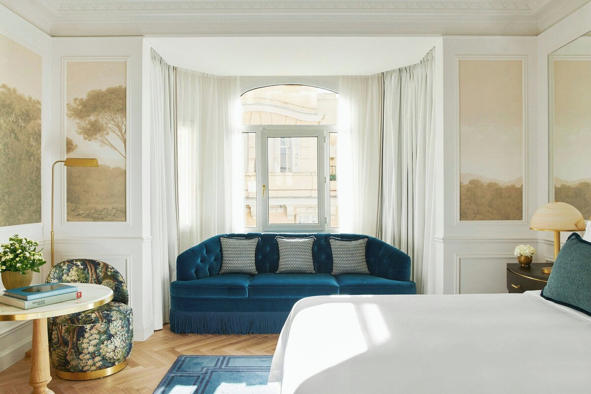 Una stanza con un letto, un divano blu, un tavolino con una lampada e una vista dalla finestra.