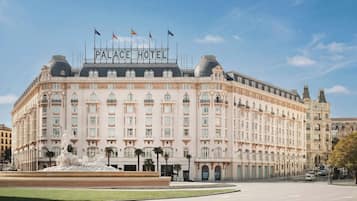 Un edificio grande e histórico con el letrero 'PALACE HOTEL' en el techo, que presenta arquitectura clásica con múltiples balcones y una fuente central.
