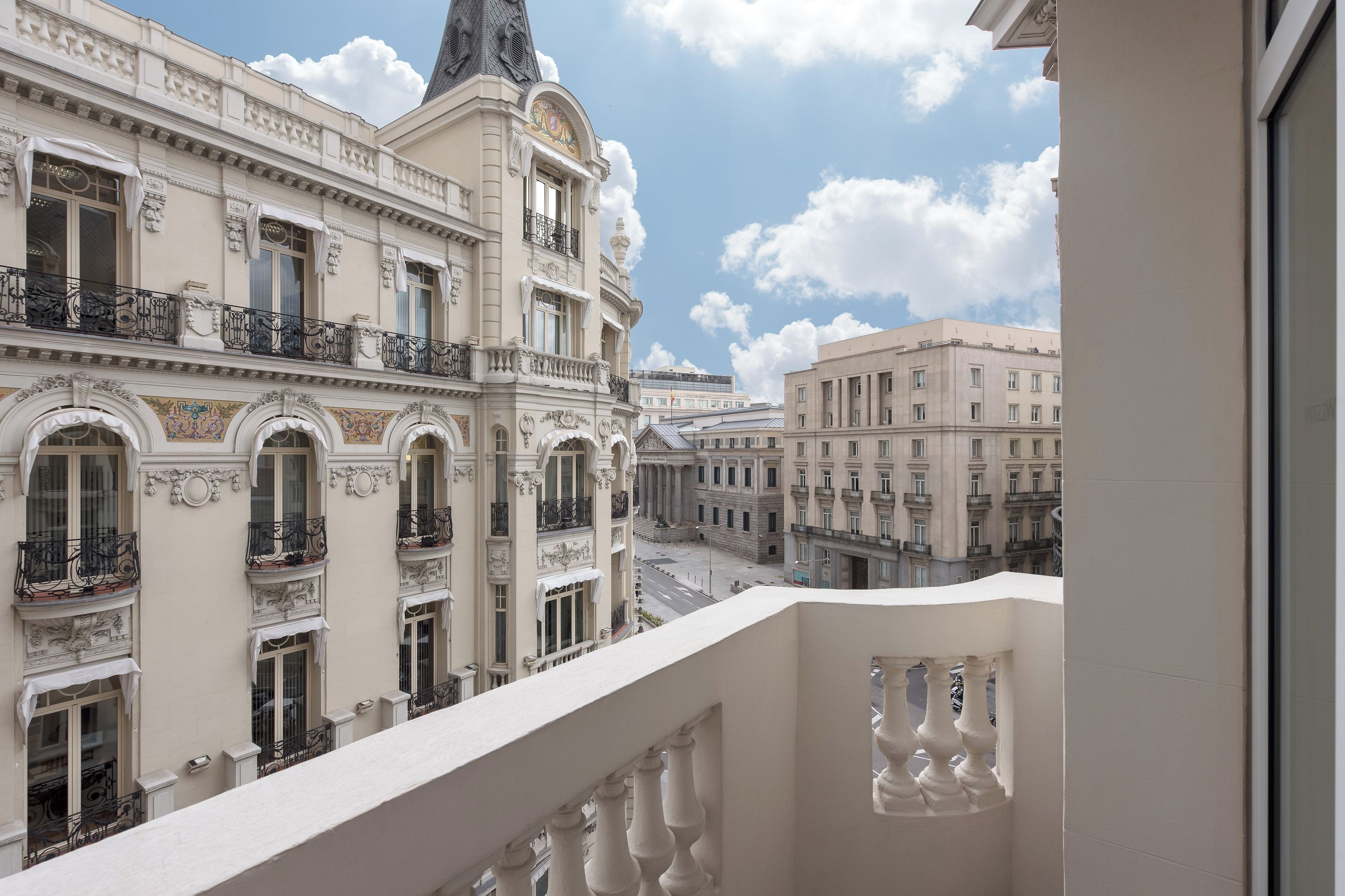 A view from a balcony overlooking a street with classical architecture, including ornate balconies and a clock tower.