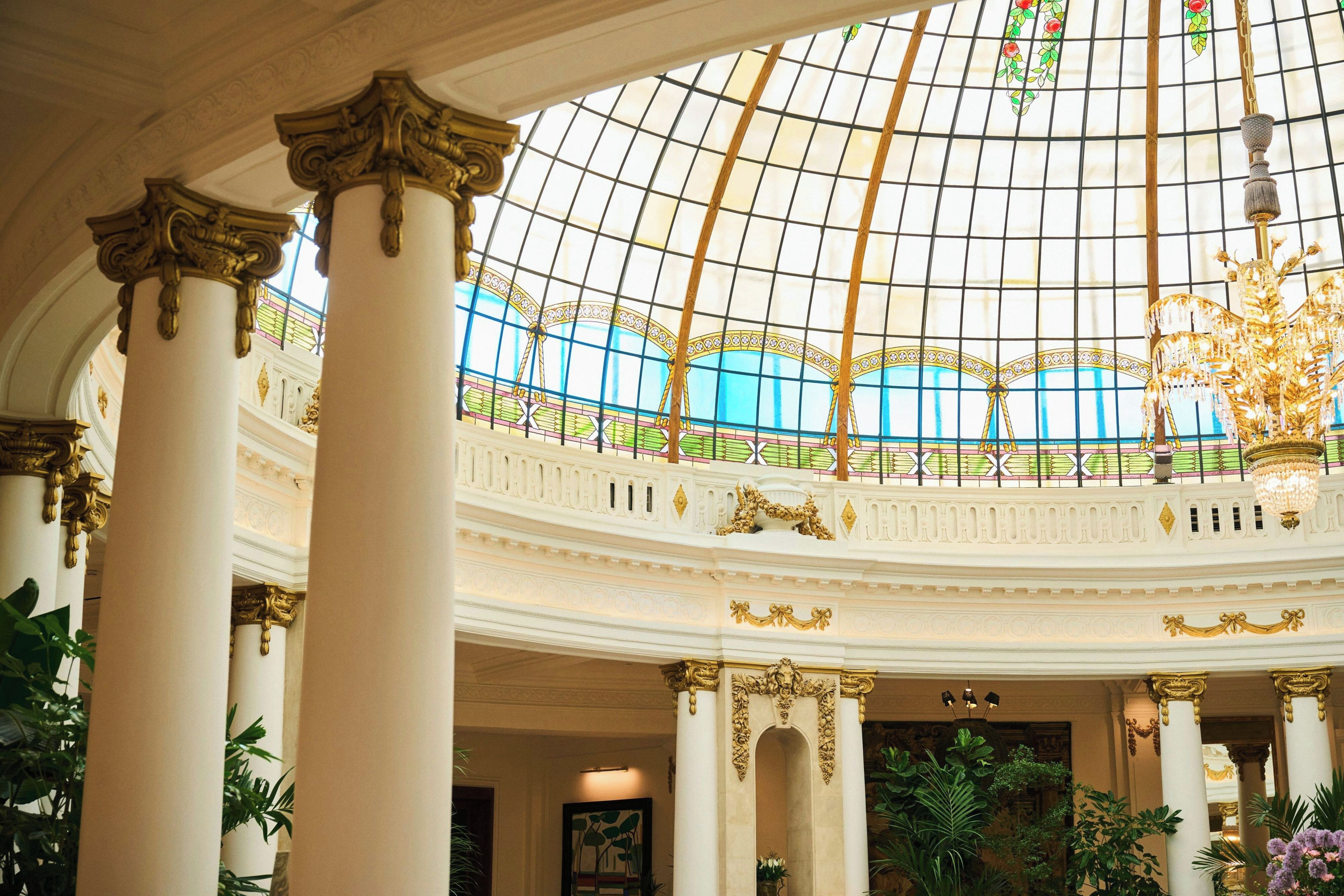 Un interior imponente con techo de vidrio abovedado, columnas ornamentales y un candelabro central.