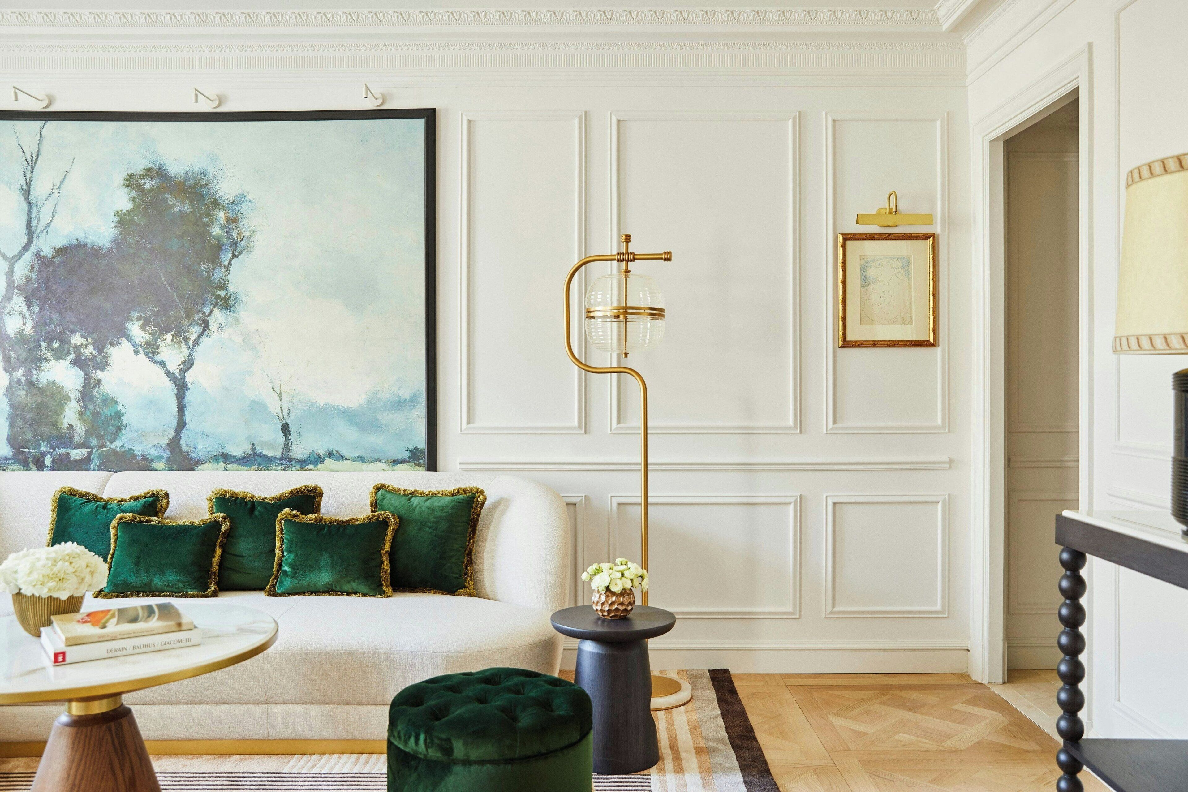 Un salon avec un canapé blanc, des coussins verts, une table basse ronde et un grand lampadaire.
