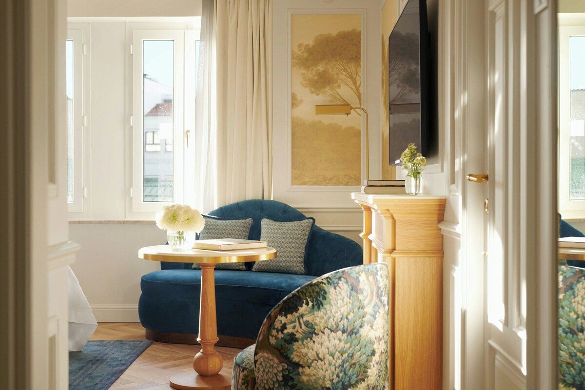 Una stanza con un divano blu, un tavolino rotondo in legno con un vaso e una sedia con motivo floreale.