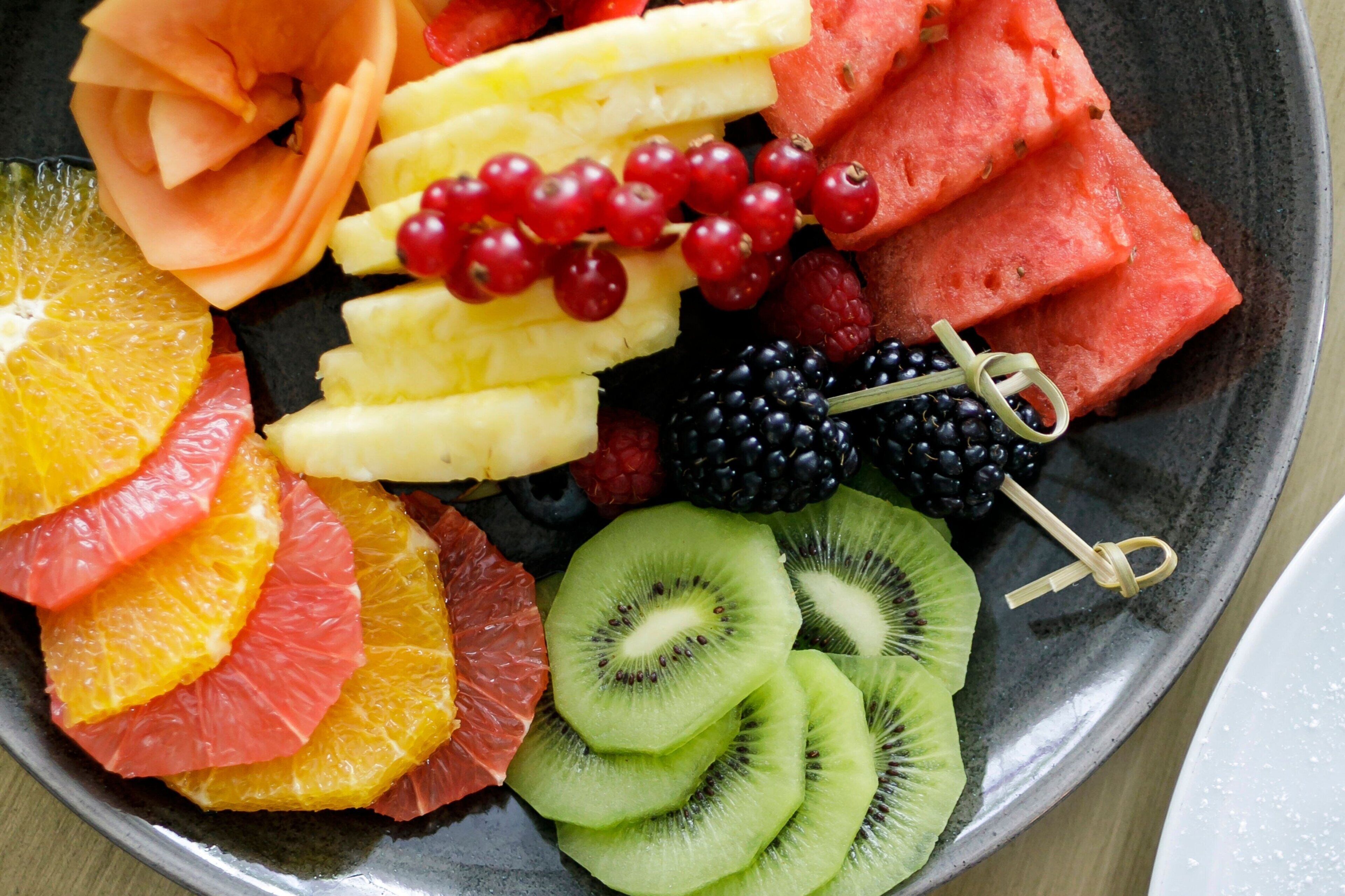 Una bandeja de frutas con diversas frutas cortadas, incluyendo naranjas, kiwi, sandía y frutos rojos.