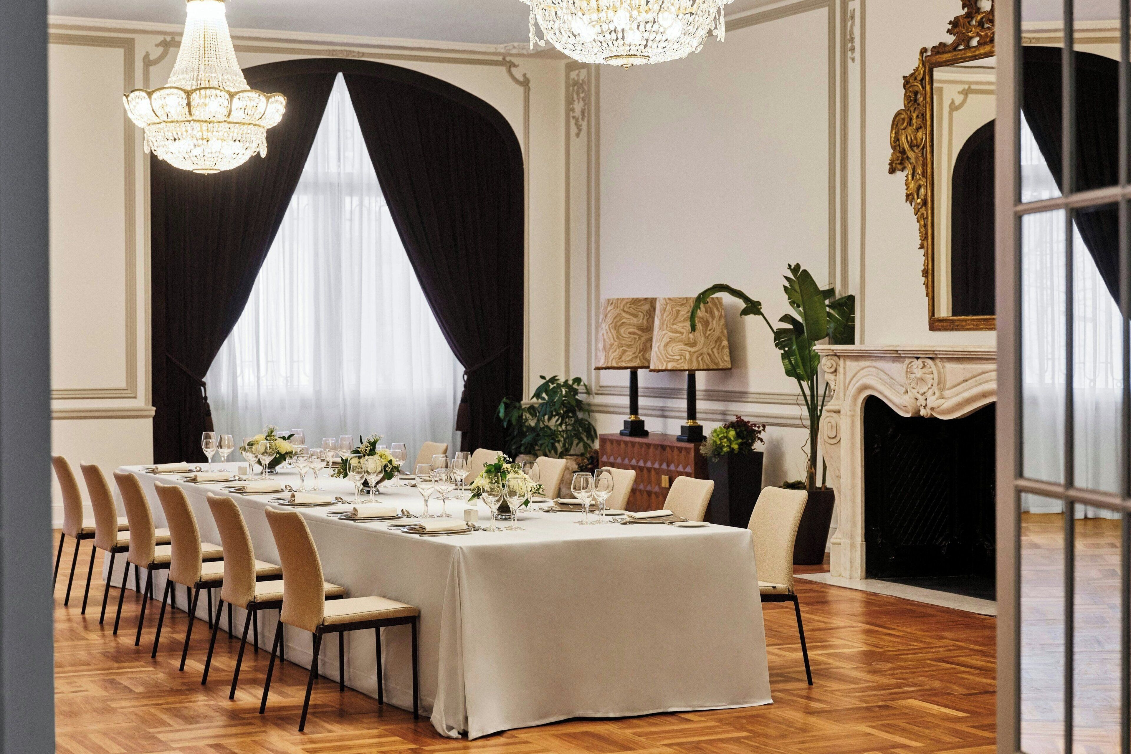 A formal dining room with a long table set for a meal, elegant chandeliers, and a fireplace.