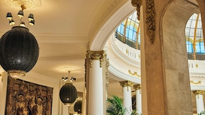 Un interior imponente con columnas decoradas, una gran lámpara de araña y un mural.